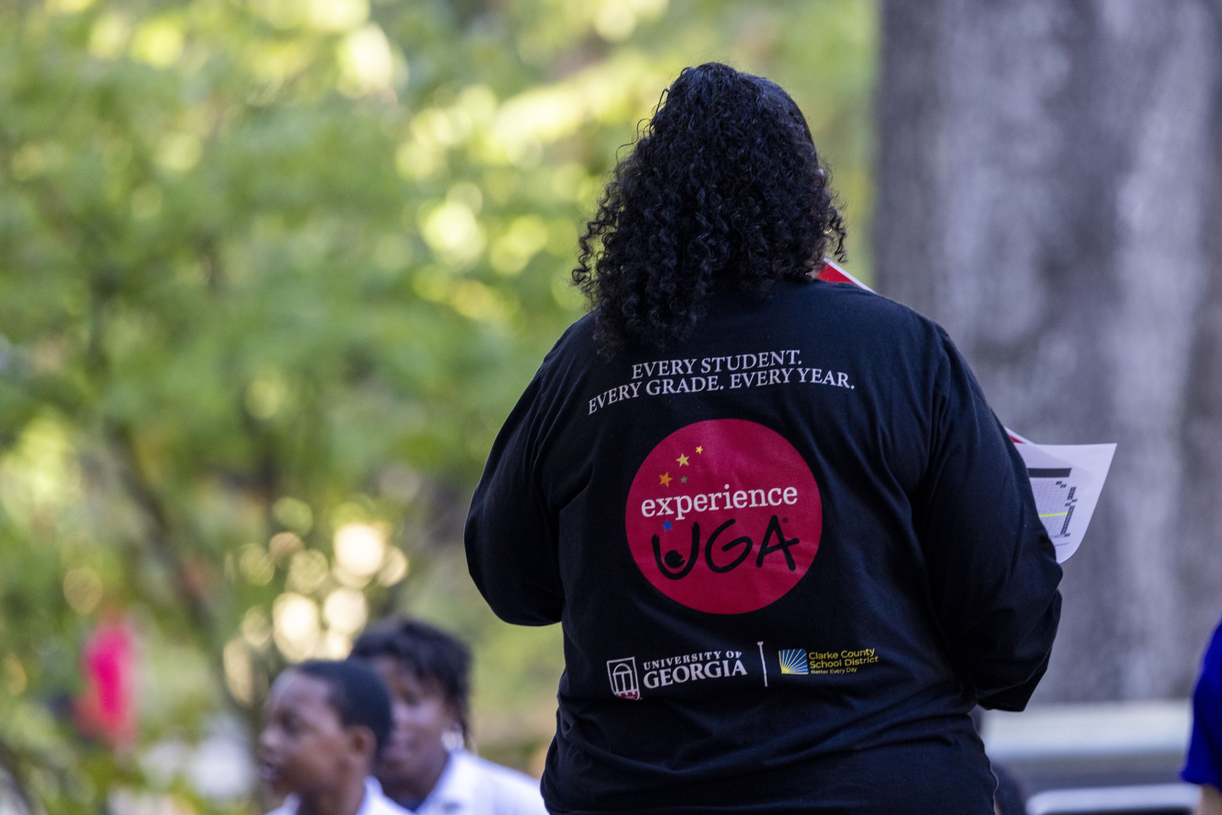An Experience UGA Ambassador standing with their back to the camera - the back of their shirt displays Experience UGA's logo with the text - Every Student / Every Grade / Every Year 