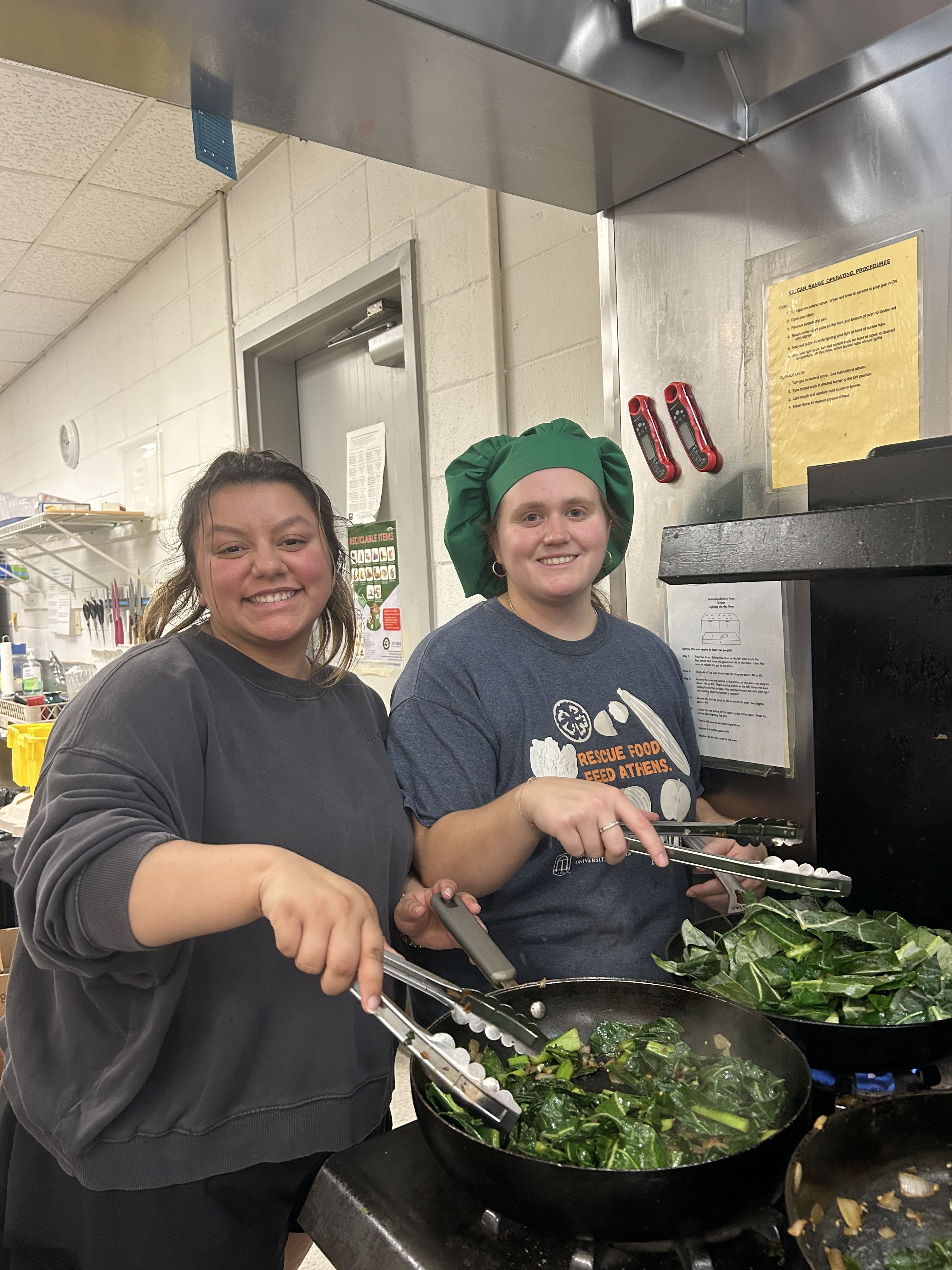 Campus Kitchen graduate student Caitlin Grdinich and student intern Jimena Ruano smile while cooking a meal over the stove