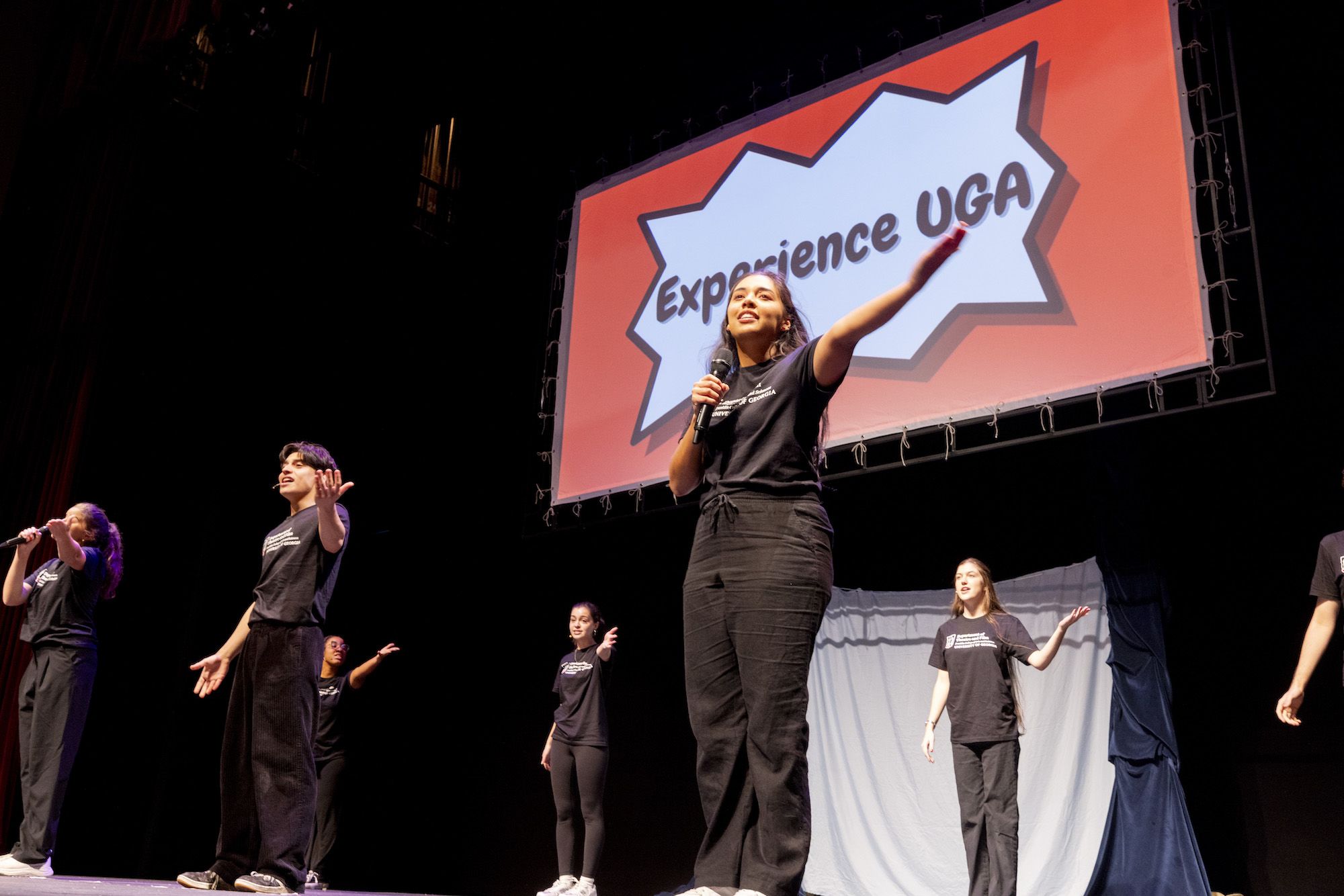 A UGA theatre student holding a microphone performs on stage for an Experience UGA trip