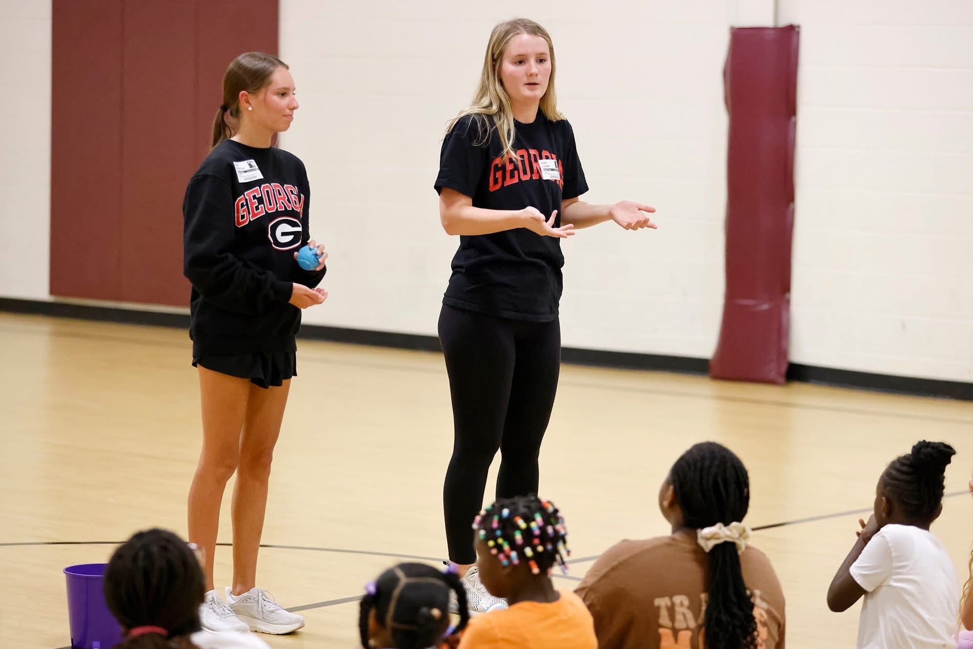 Two Coaching4Success mentors talk to a group of elementary school children in the basketball gym.