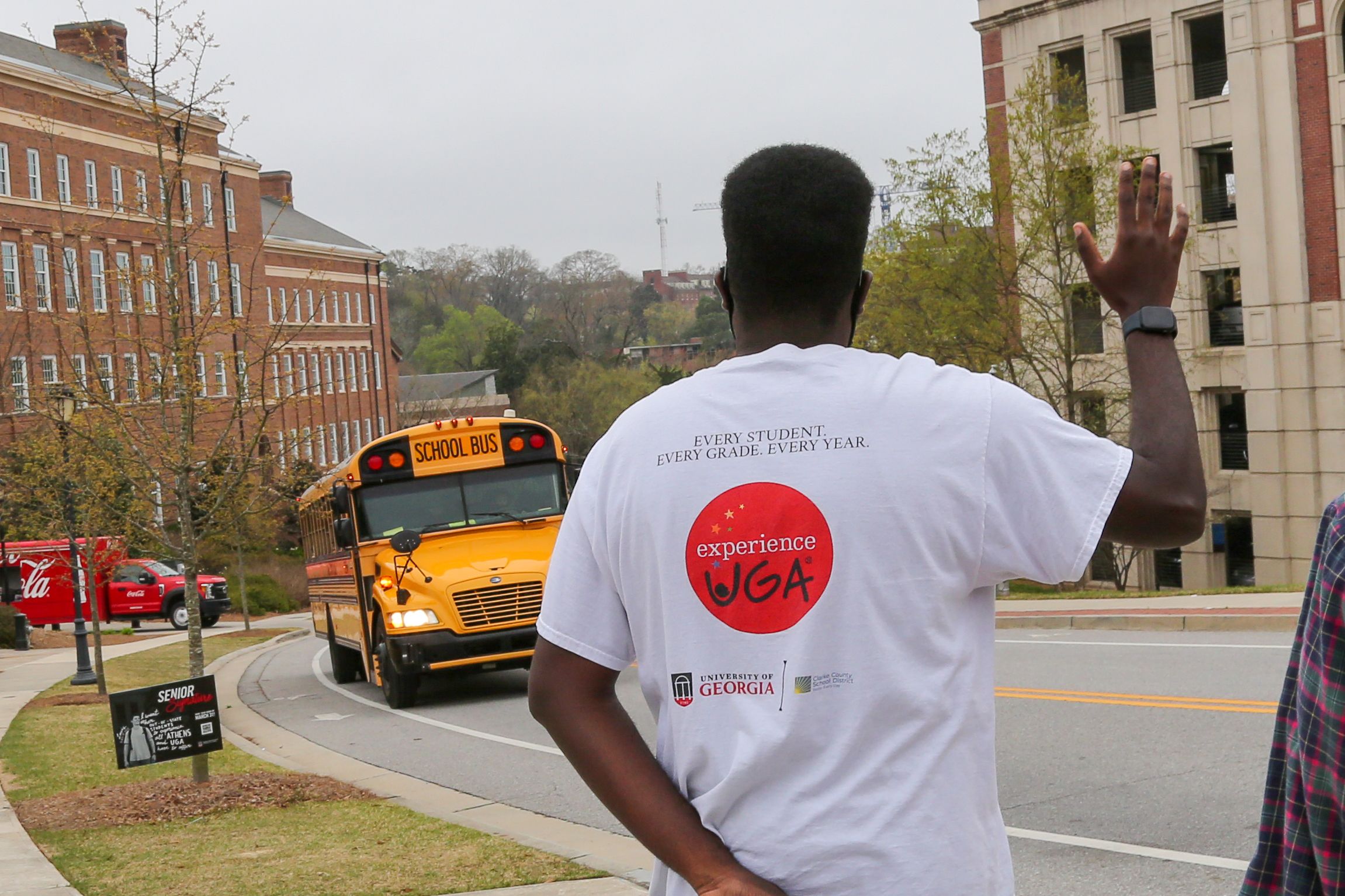 A UGA student waves as a school bus approaches for a field trip on campus.
