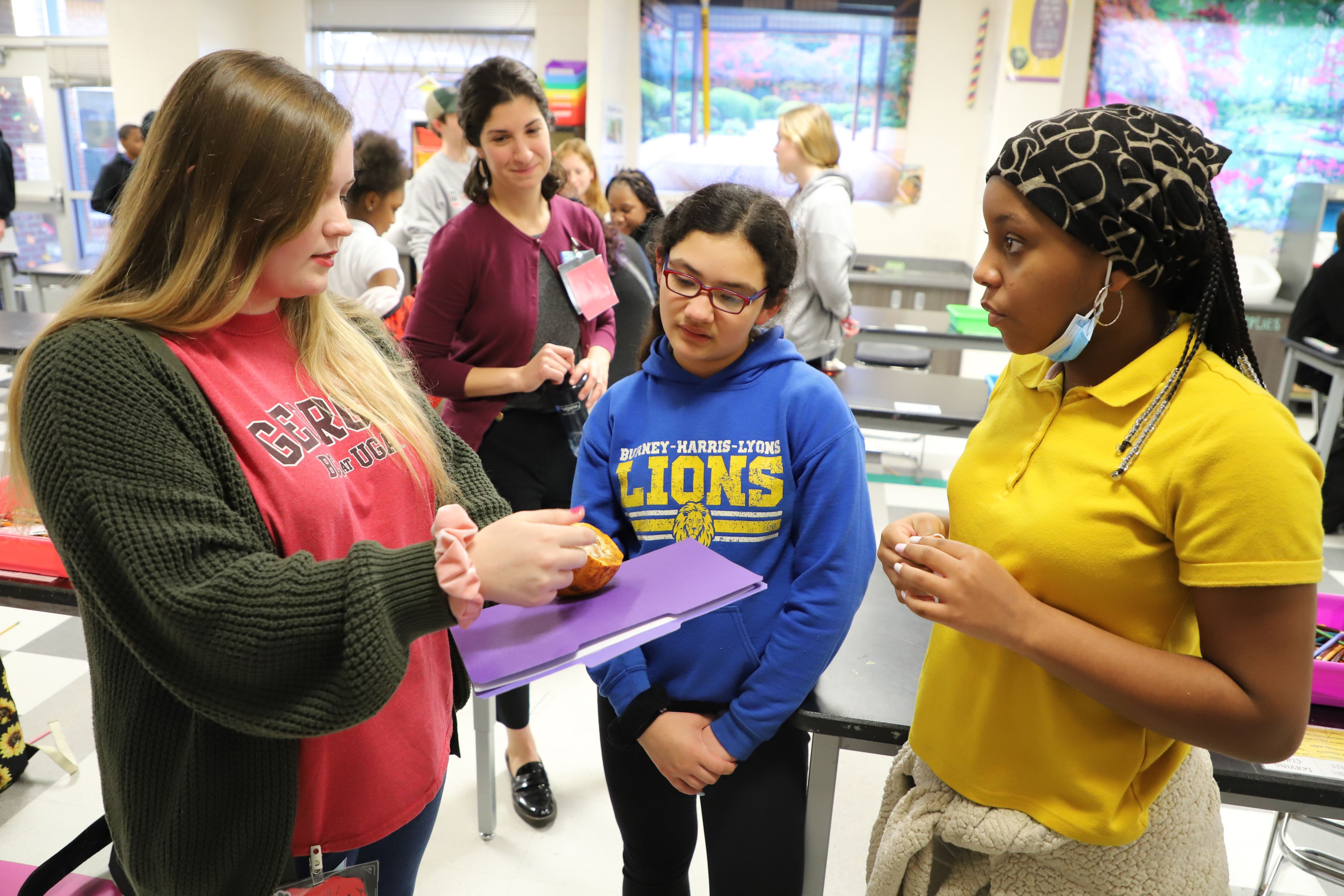 A UGA student shows middle school students what a cacao fruit looks like.